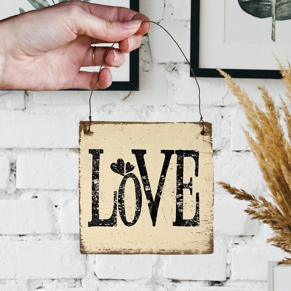 A hand holding a square wooden sign with the word LOVE